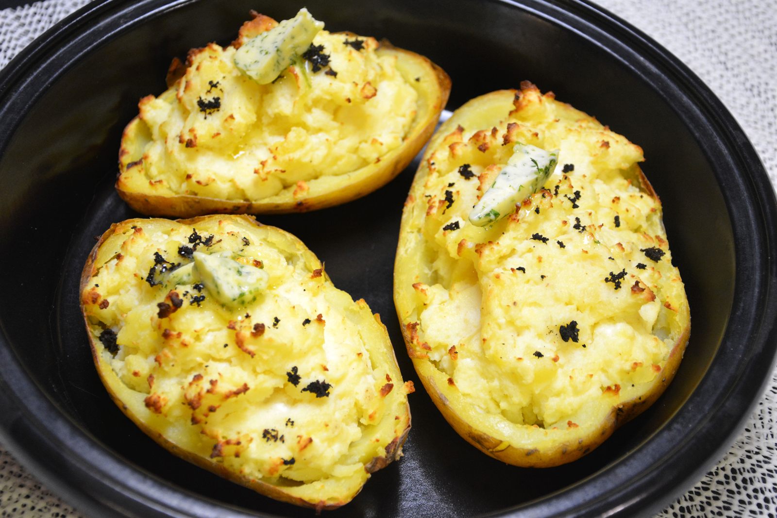 Patatas rellenas al horno con queso feta y mantequilla de hierbas en una fuente negra