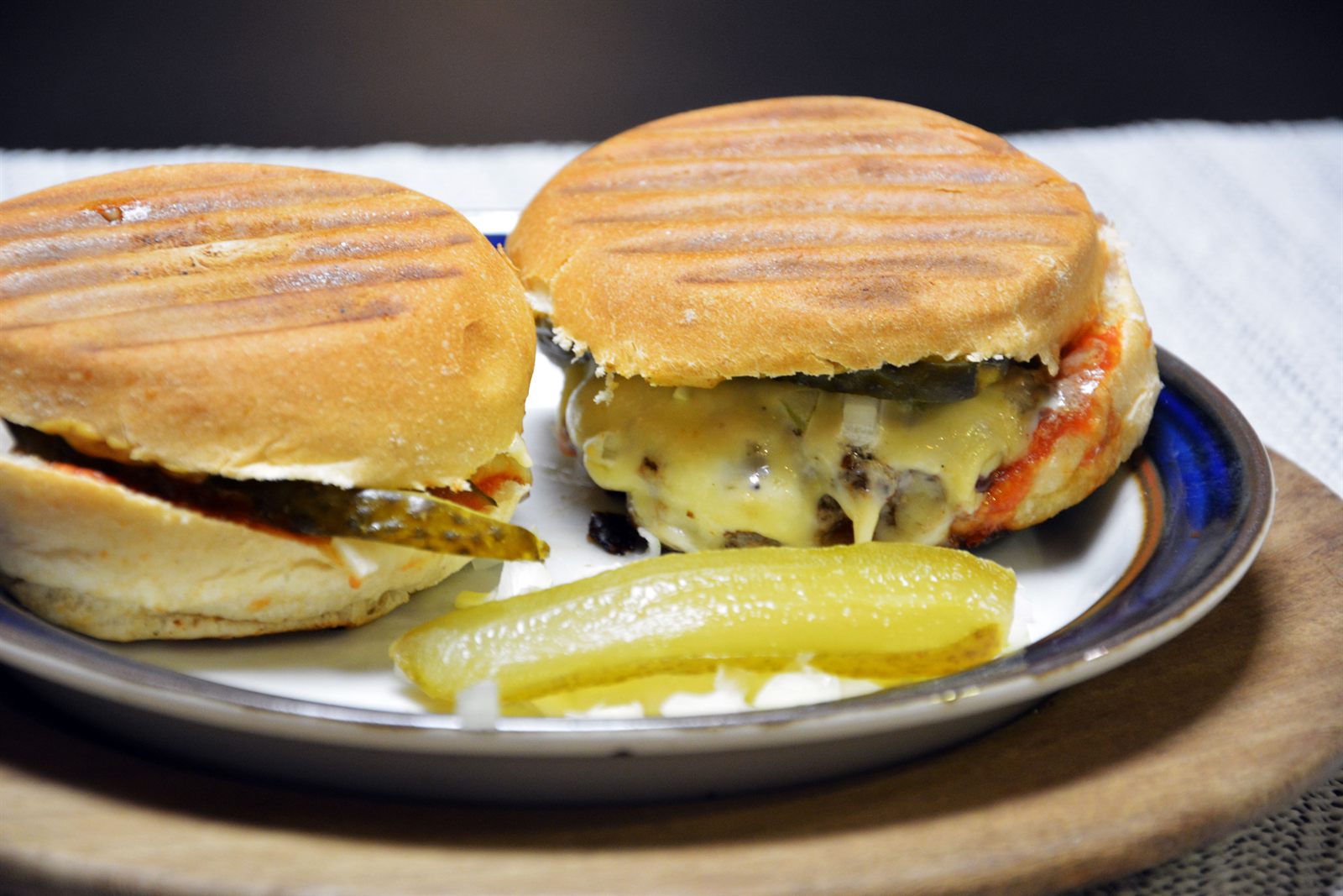 Dos hamburguesas caseras con marcas de plancha en el pan, queso fundido y pepinillo en un plato