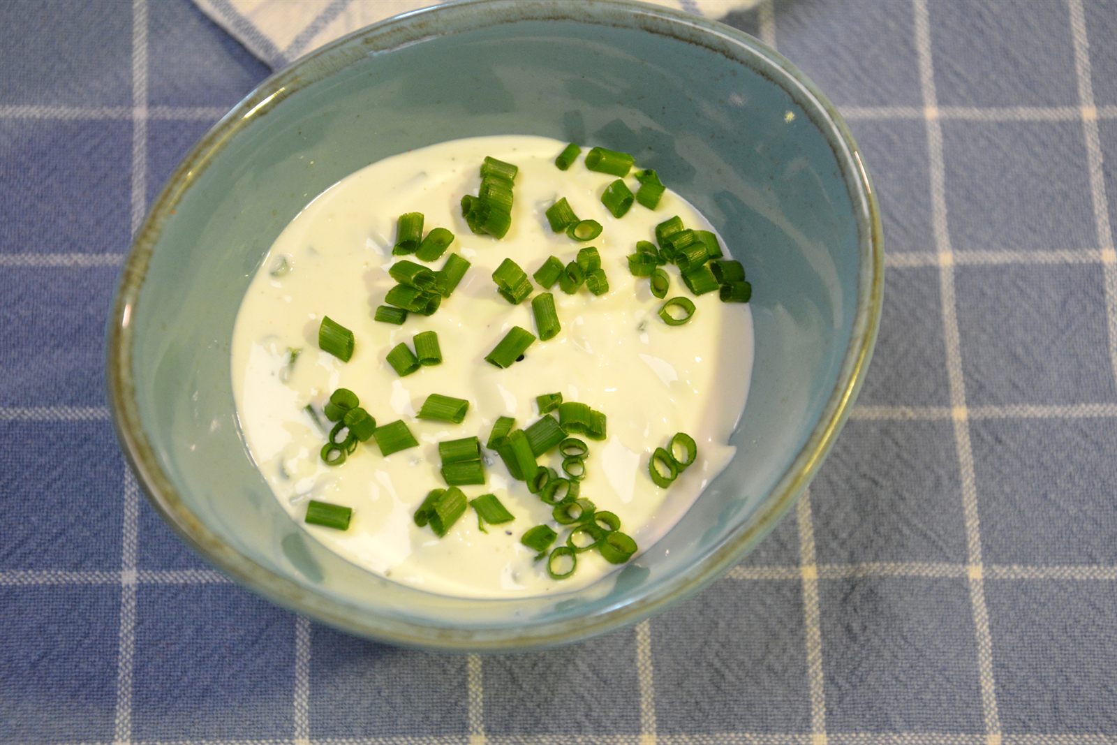 Salsa cremosa para ensalada con cebollino en un cuenco turquesa sobre un paño de cocina de cuadros azules