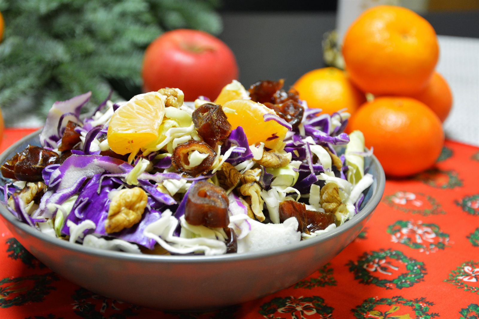 Ensalada de Navidad con endibias y lombarda en juliana, dátiles, nueces y gajos de clementina en un bol metálico sobre un mantel navideño rojo